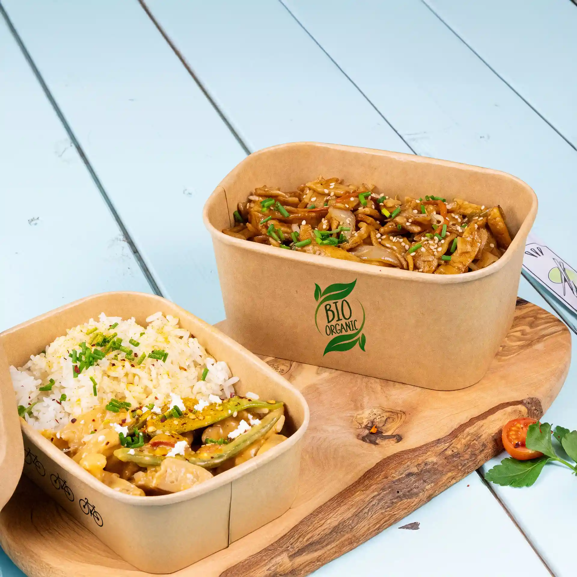 Bols rectangulaires marron avec du riz et des nouilles, placés sur une planche en bois avec un fond bleu clair.