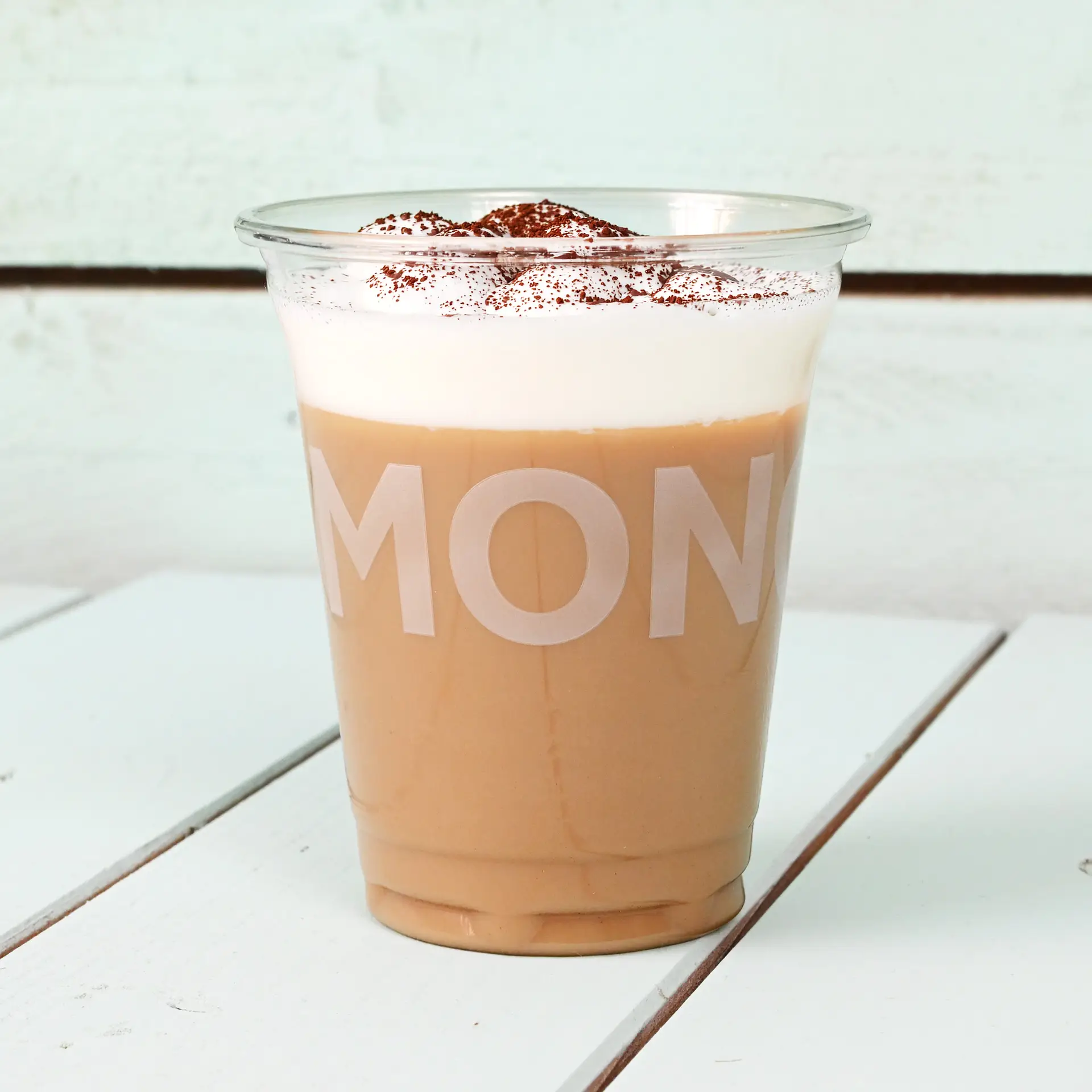 Gobelet rPET transparent rempli de café glacé, surmonté de crème fouettée et de cacao, sur une surface en bois.
