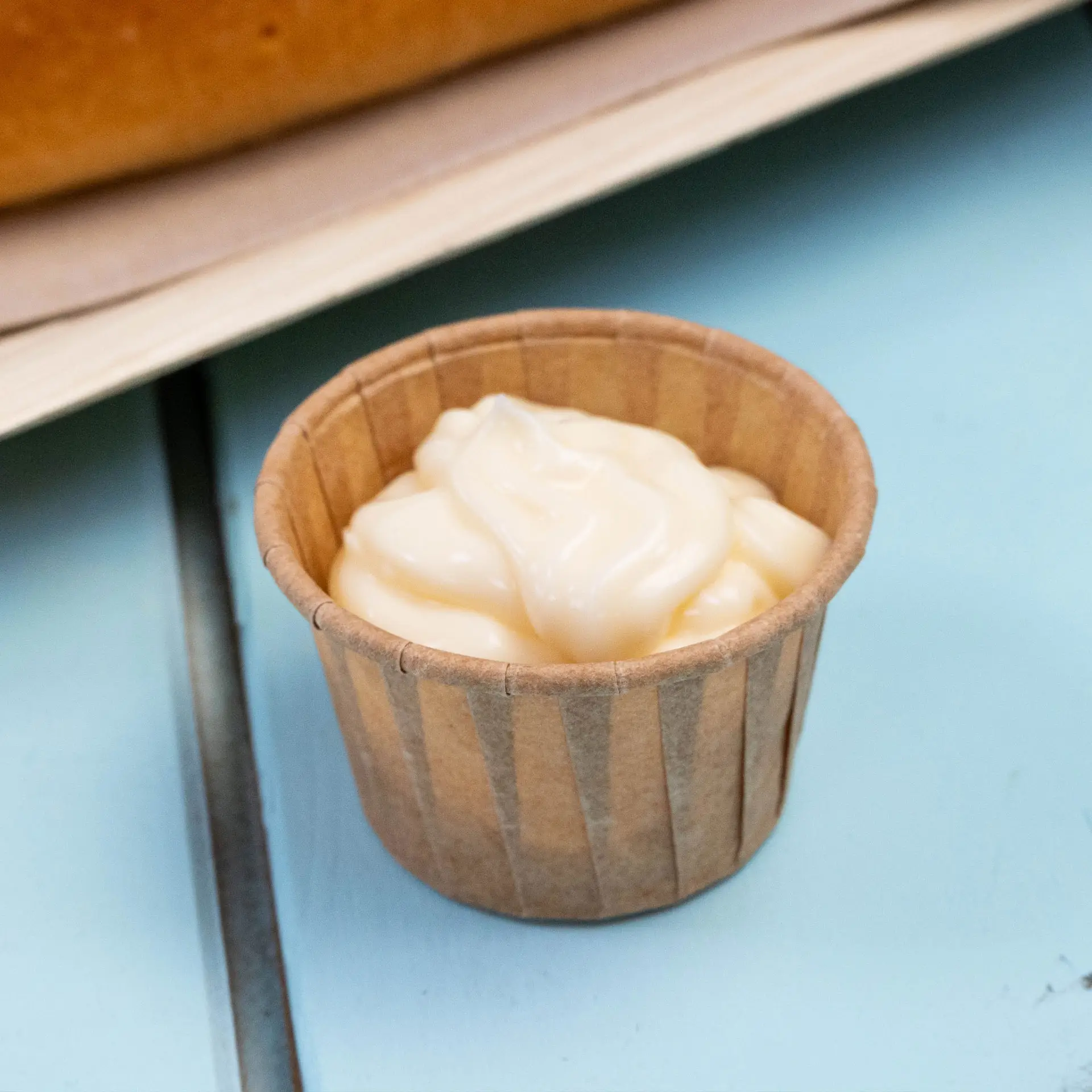 Petit gobelet en papier brun contenant un dip crémeux, idéal pour les sauces et les portions de dégustation, sur une surface bleue.