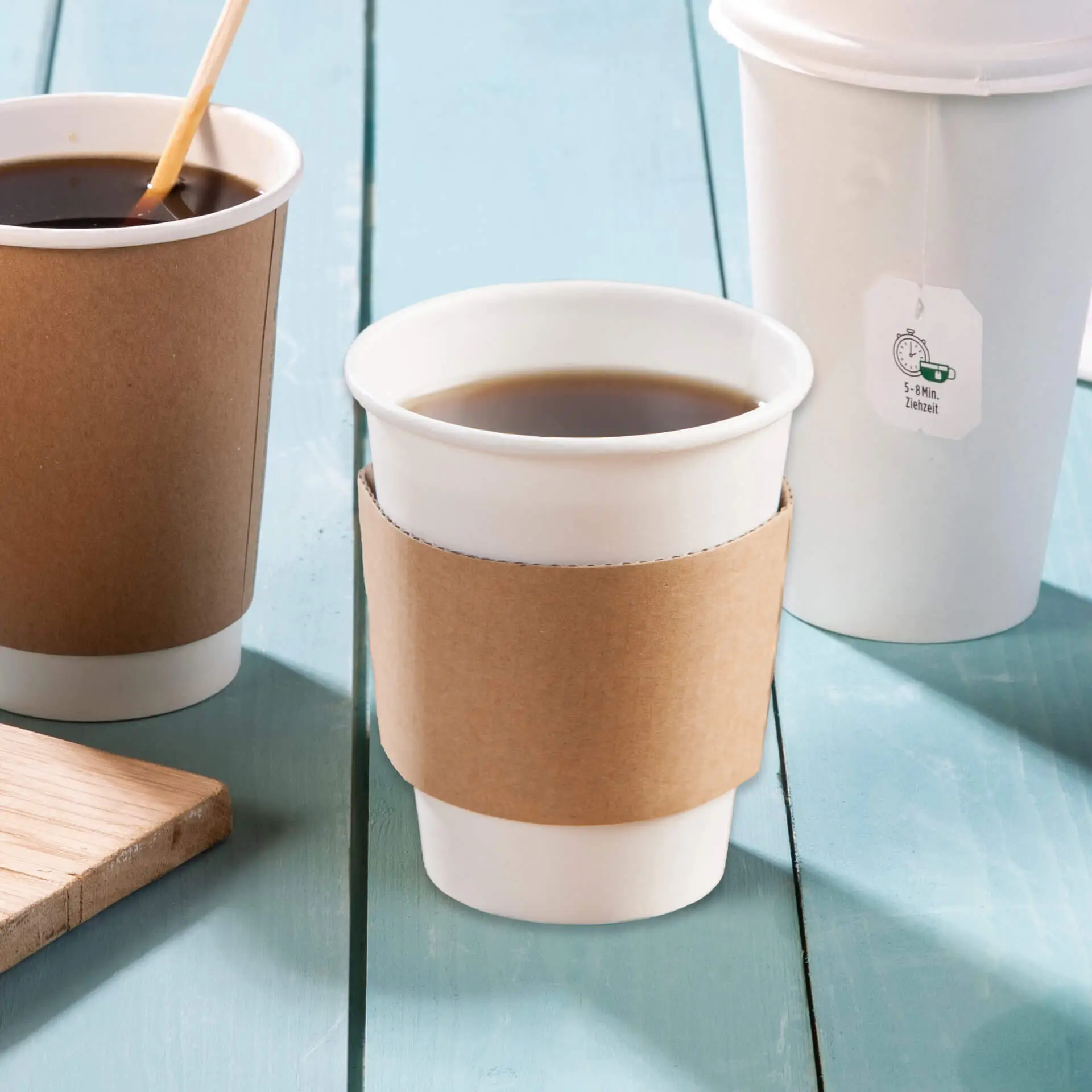 Manchon en carton marron sur une tasse en papier, améliorant la prise et la protection contre la chaleur, avec des tasses supplémentaires à proximité sur une surface en bois bleu.