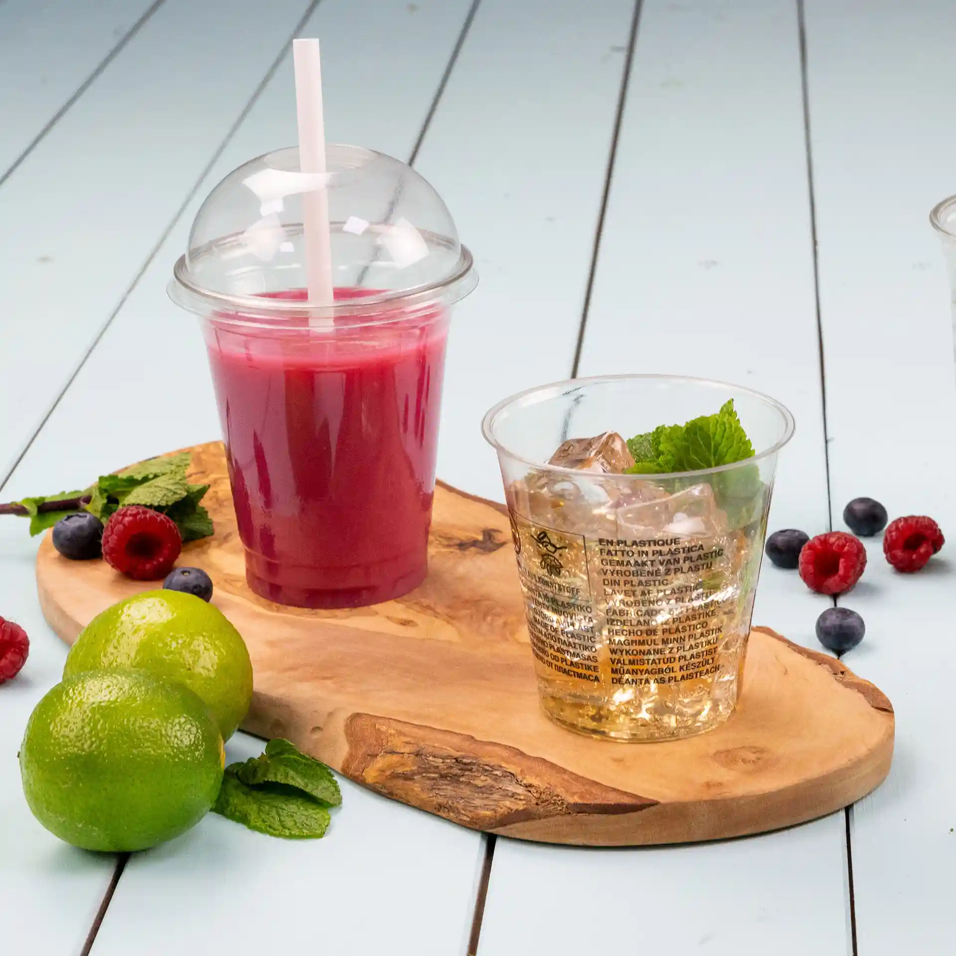 Image d'une planche de service en bois avec un gobelet rPET transparent de 12 oz rempli d'une boisson rose et un second gobelet clair avec de la glace et de la menthe.