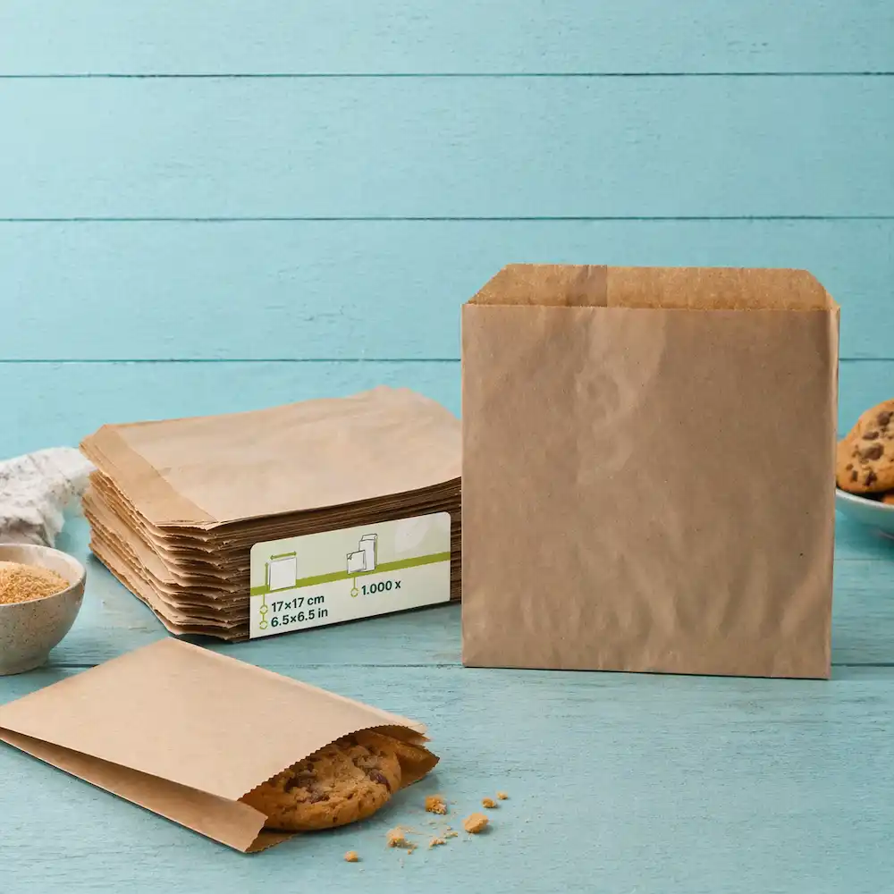 Sacs en papier bruns empilés à côté d'un sac ouvert contenant un biscuit, sur un fond en bois bleu.