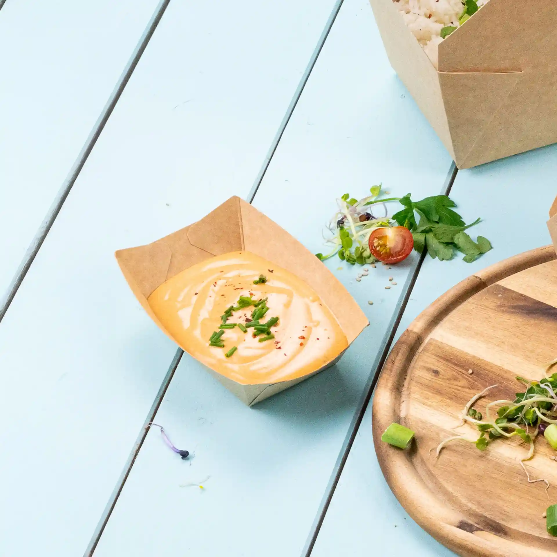 Plateau à snacks en carton brun avec une sauce crémeuse garnie de ciboulette hachée, posé sur une surface bleu clair.
