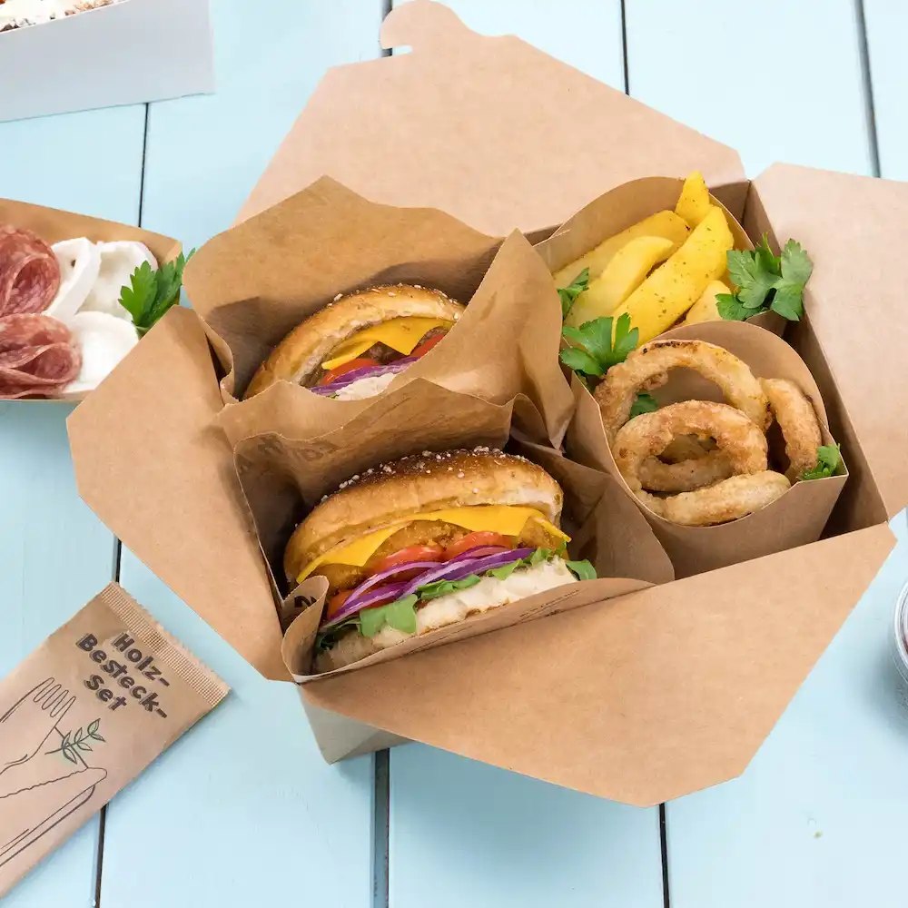 Deux hamburgers avec fromage, laitue, tomate et oignon dans une boîte à emporter, accompagnés d'anneaux d'oignon et de frites.