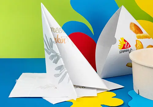 Serviettes imprimées personnalisées disposées sur une table avec une tasse de café, un dessert et un verre de baies. Serviettes en papier décorées visibles.