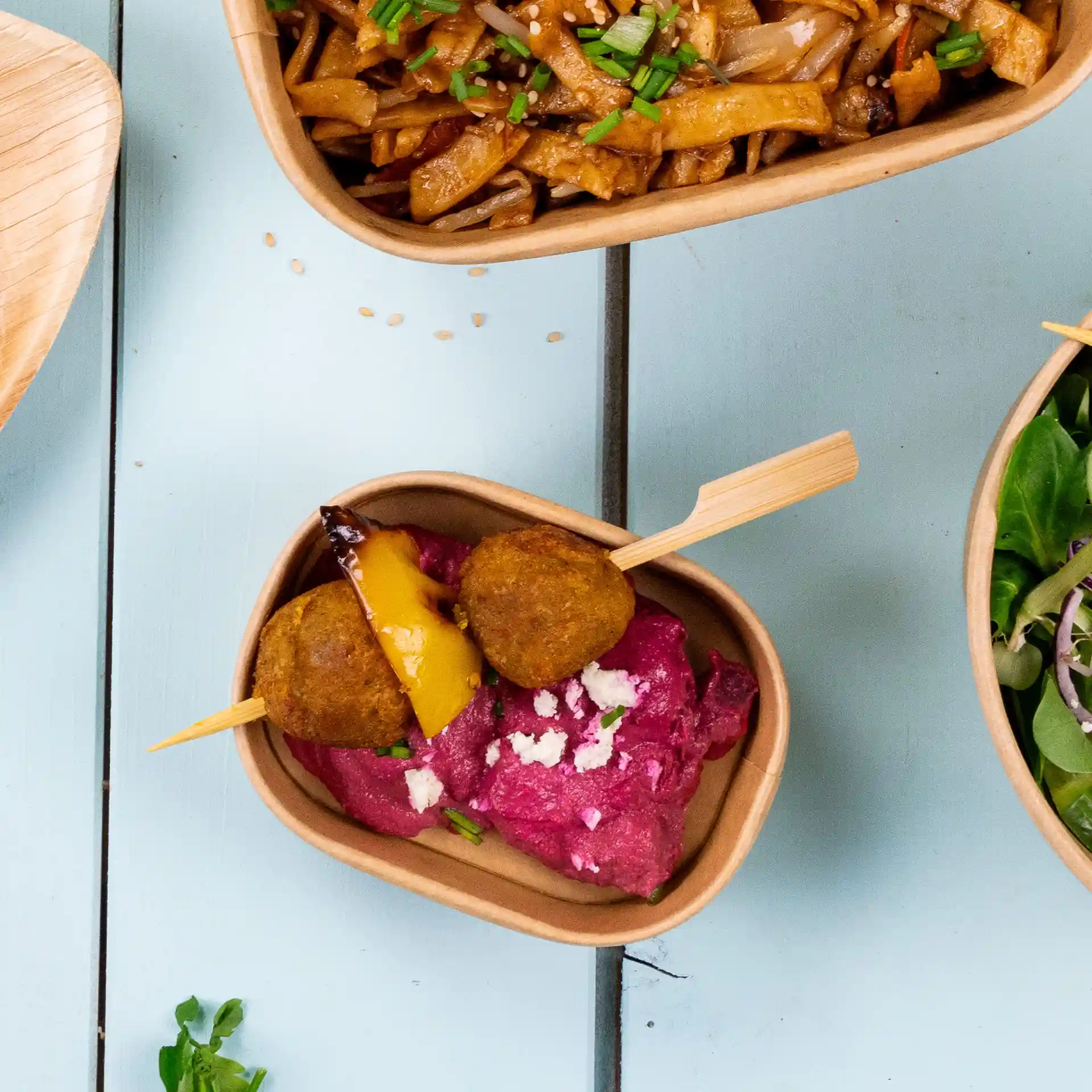 Brochettes en bambou avec deux boules dorées et un morceau de poivron jaune sur un lit de dip rose dans un bol marron.