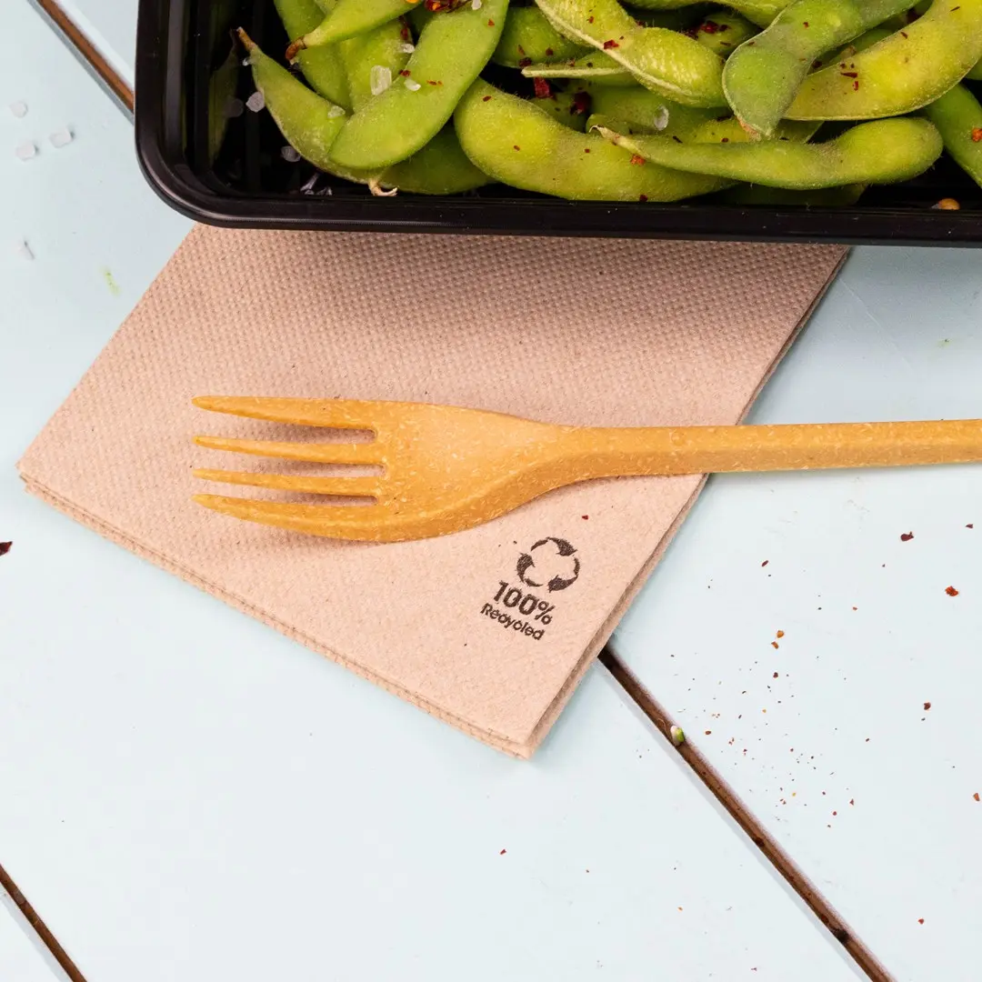 Serviette brune avec une fourchette jaune posée dessus, à côté d'un contenant noir de fèves edamame.