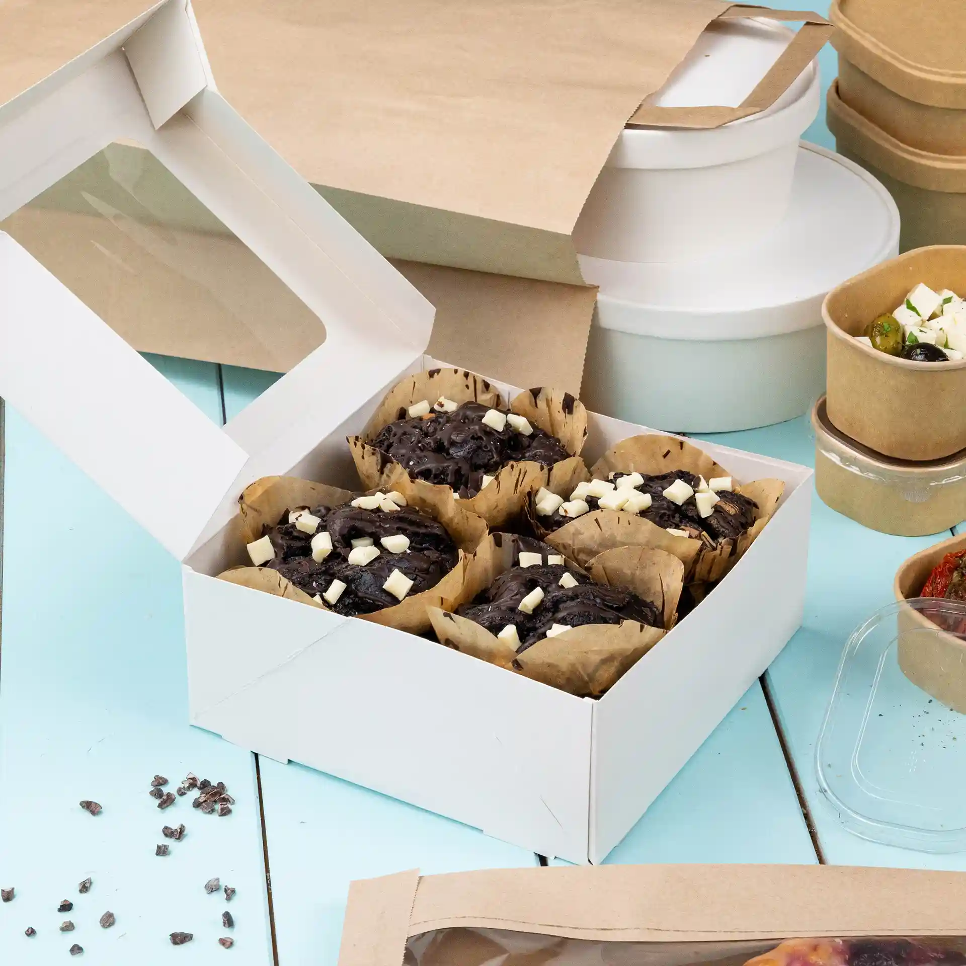 Boîte en carton blanc avec une fenêtre transparente contenant plusieurs muffins au chocolat garnis de morceaux de chocolat blanc.