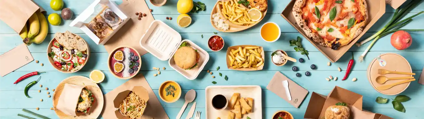 Une variété d'aliments disposés sur une surface bleue, comprenant des pizzas, des salades, des burgers et des desserts dans des contenants.
