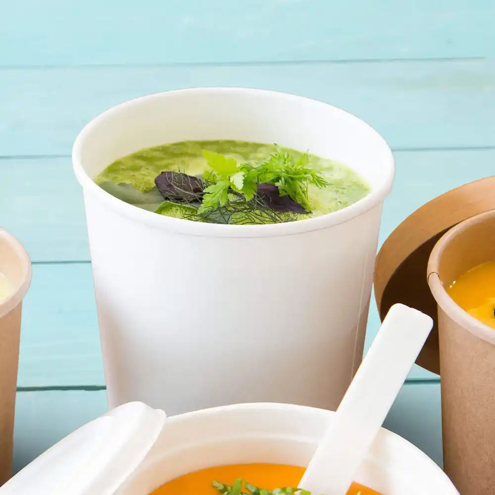 Bol de soupe blanc rempli de soupe verte et garni d'herbes, entouré d'autres récipients.