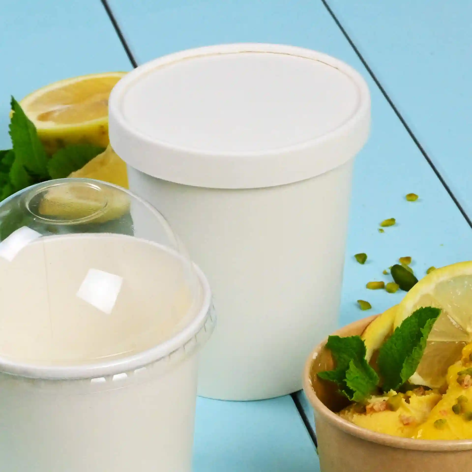 Couvercle en papier rond blanc pour pots de glace, placé à côté d'un pot blanc et d'une tasse brune avec un dessert et des tranches de citron.