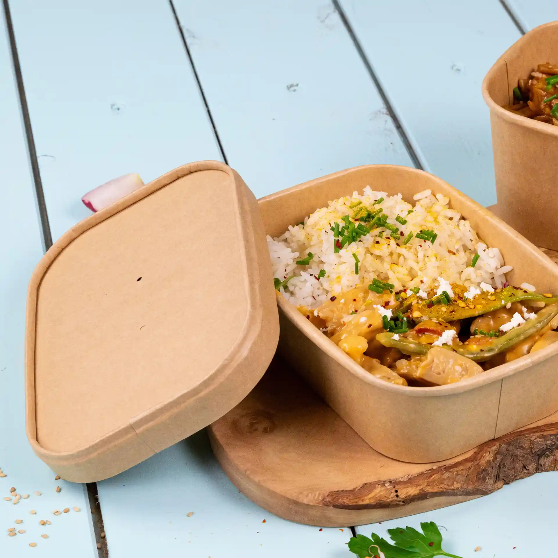 Conteneur en carton rectangulaire brun avec du riz et des légumes, partiellement ouvert sur une surface en bois.