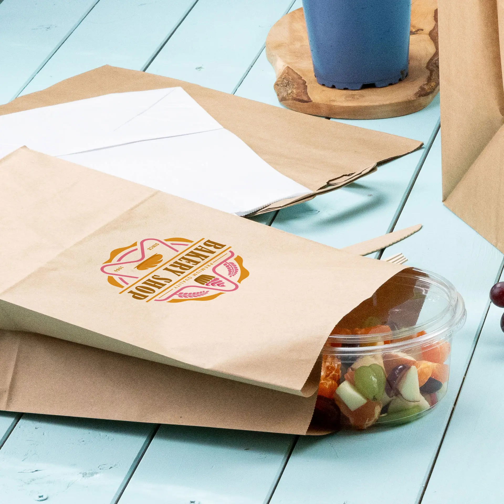Sac en papier brun imprimé avec un design circulaire vert, partiellement ouvert, avec un contenant transparent de fruits mélangés à côté.