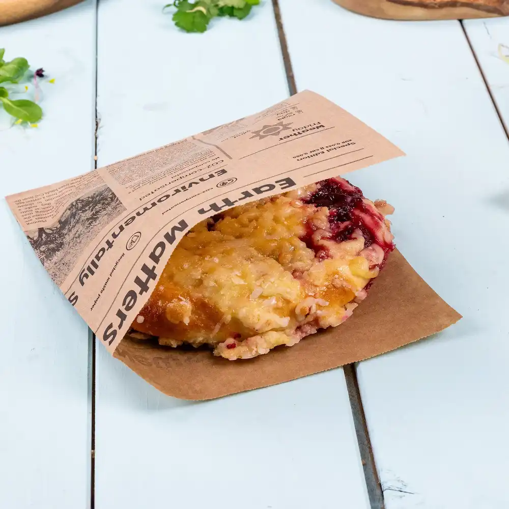 Un produit cuit avec une garniture de fruits, partiellement enveloppé dans un sac en papier brun avec une étiquette imprimée.
