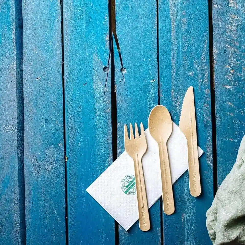 Couteau, fourchette et cuillère en papier marron disposés sur une serviette blanche sur une surface en bois bleu.
