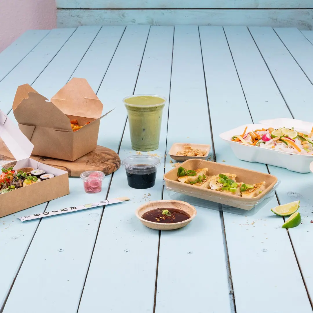 Assortiment d'aliments asiatiques sur une table en bois bleu, y compris des sushis, des dumplings, une salade et une boisson verte.