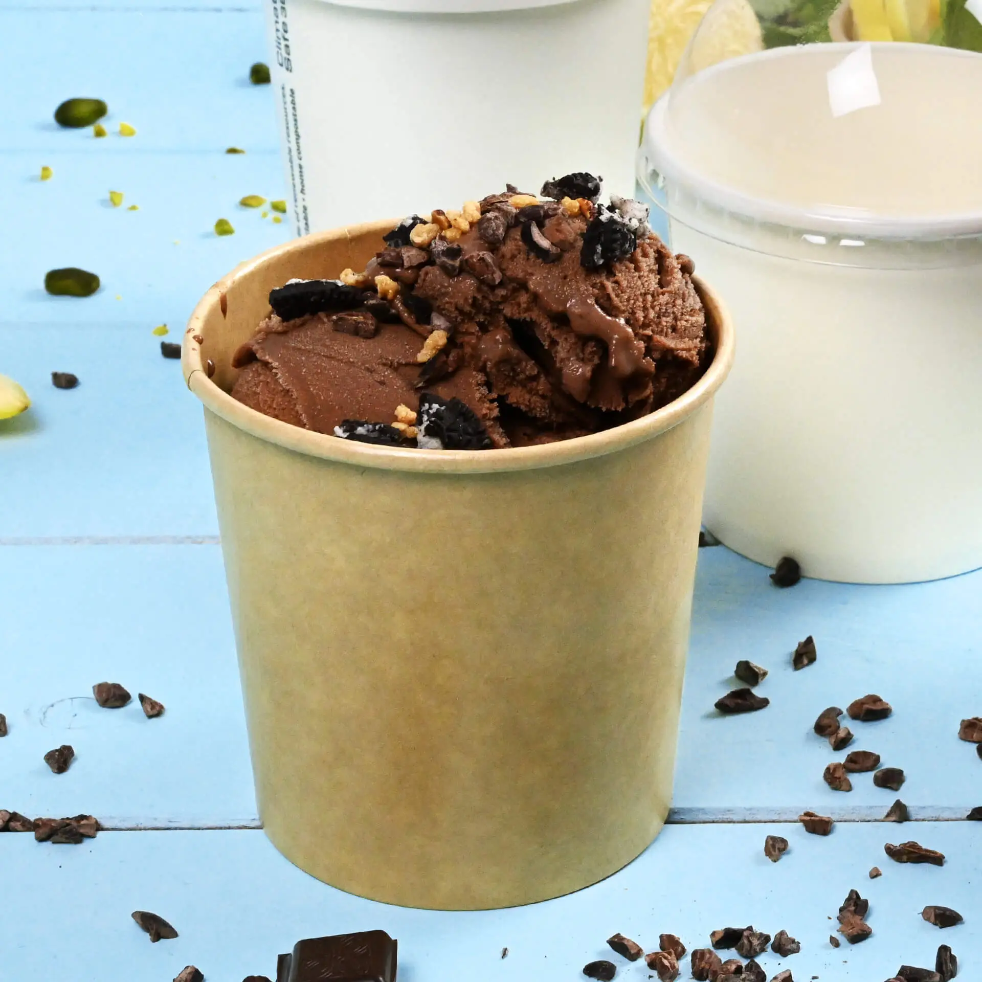 Un gobelet en papier marron rempli de glace au chocolat et de garnitures, placé sur une surface bleue avec des garnitures éparpillées.