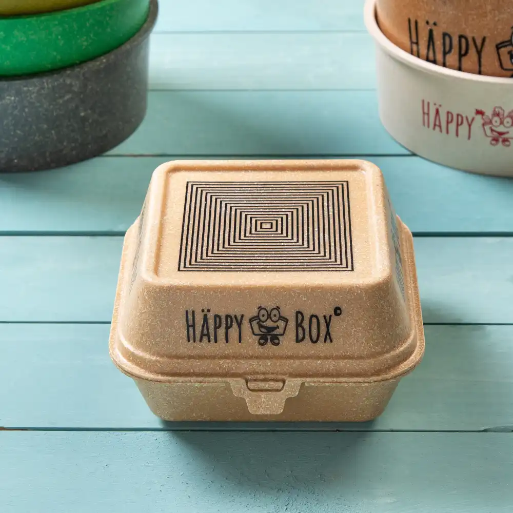 Conteneur réutilisable de forme carrée, avec un couvercle et le logo "HAPPY BOX", sur une surface en bois bleu.