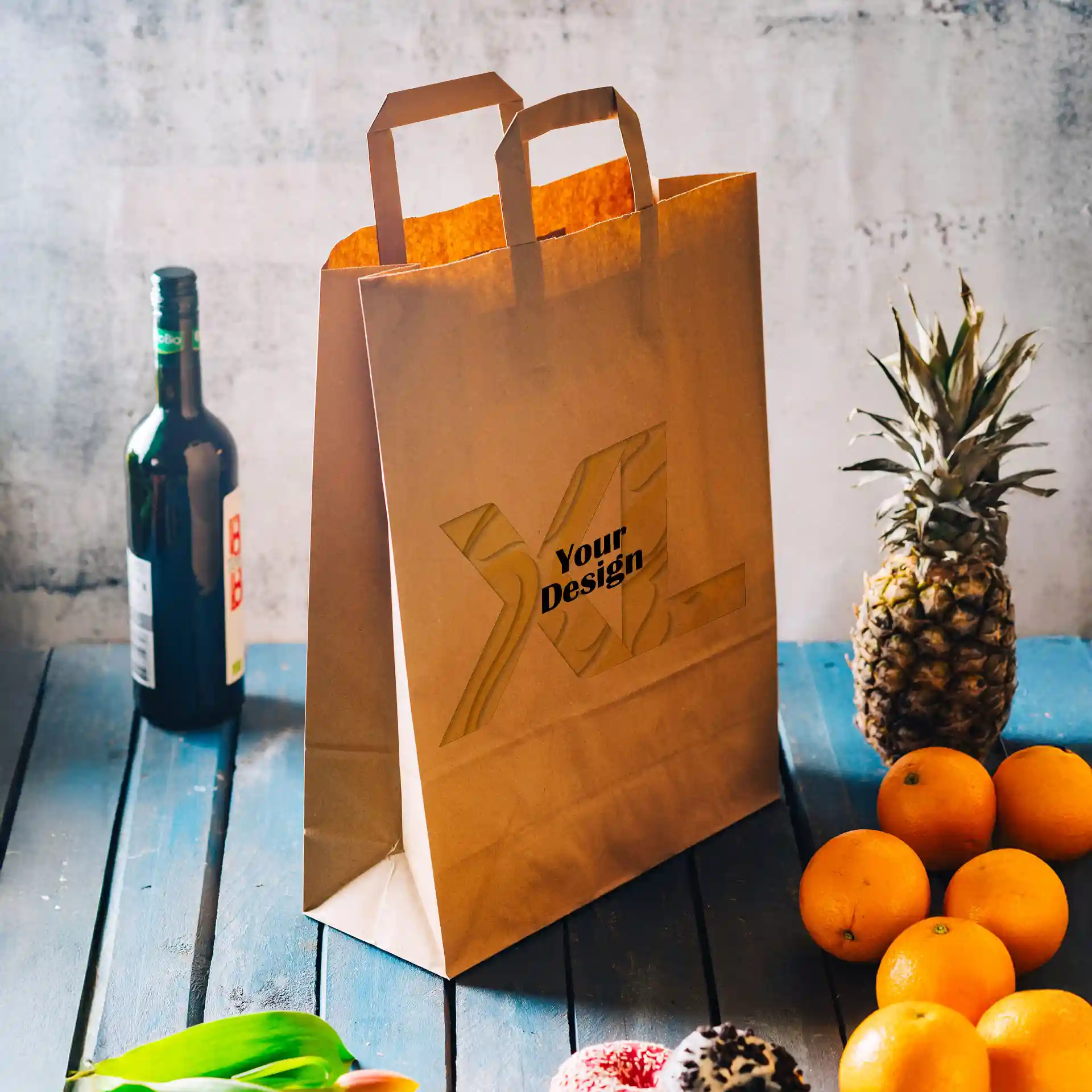 Sac en papier brun avec deux poignées, présentant une zone de design, placé à côté de fruits et d'une bouteille sur une surface en bois bleu.