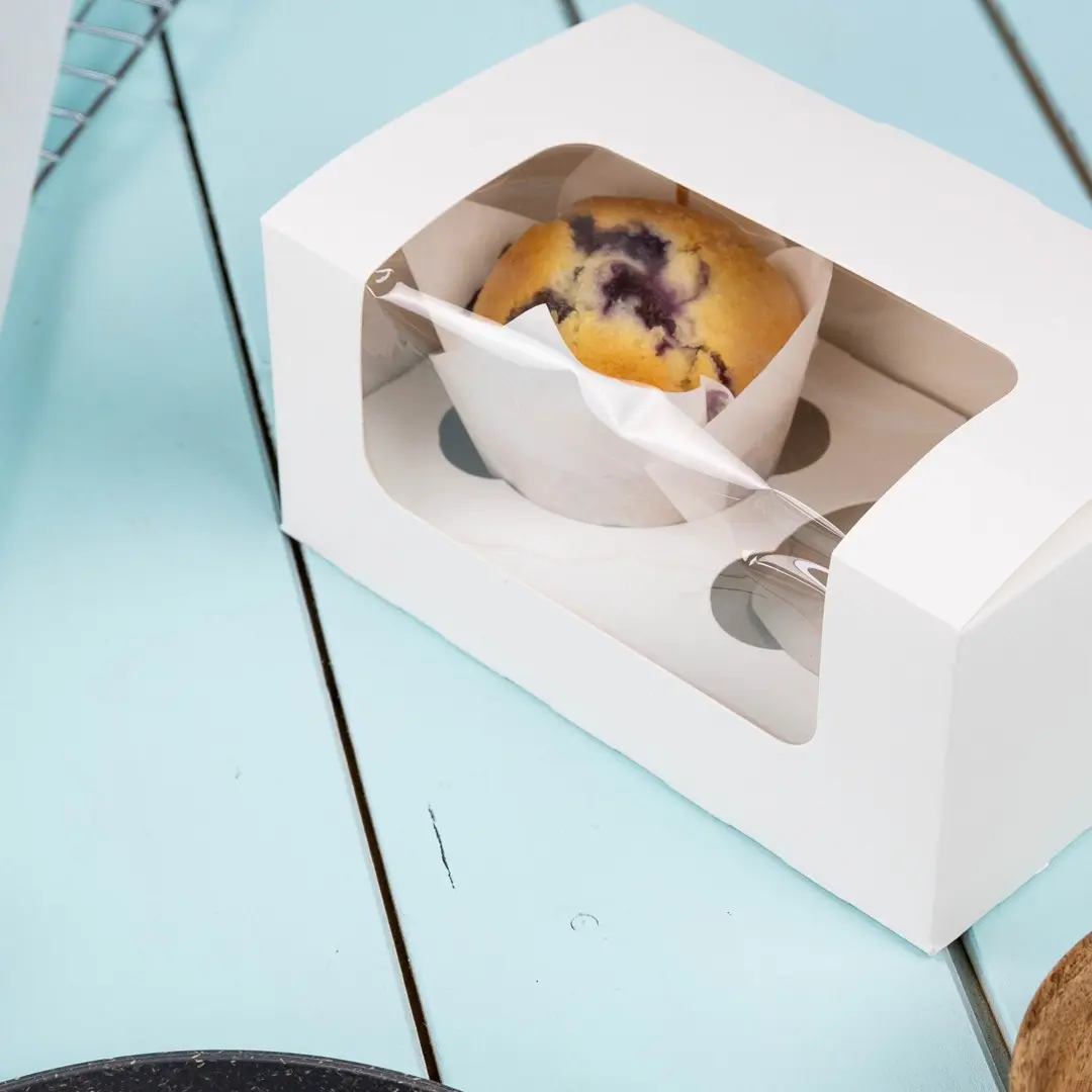 Boîte à cupcake blanche avec une fenêtre transparente affichant un muffin aux myrtilles à l'intérieur.