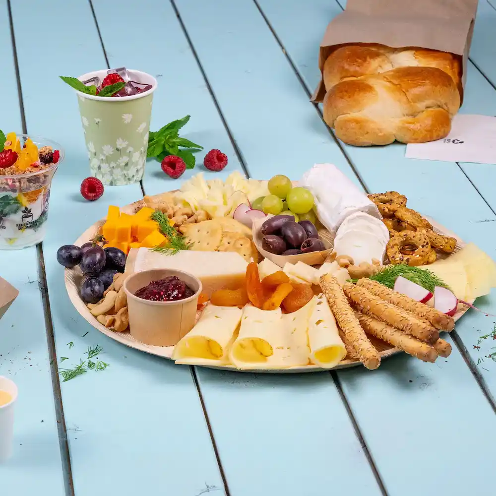 Plateau avec assortiment de fromages, crackers, fruits, noix et pain sur une surface en bois bleu.