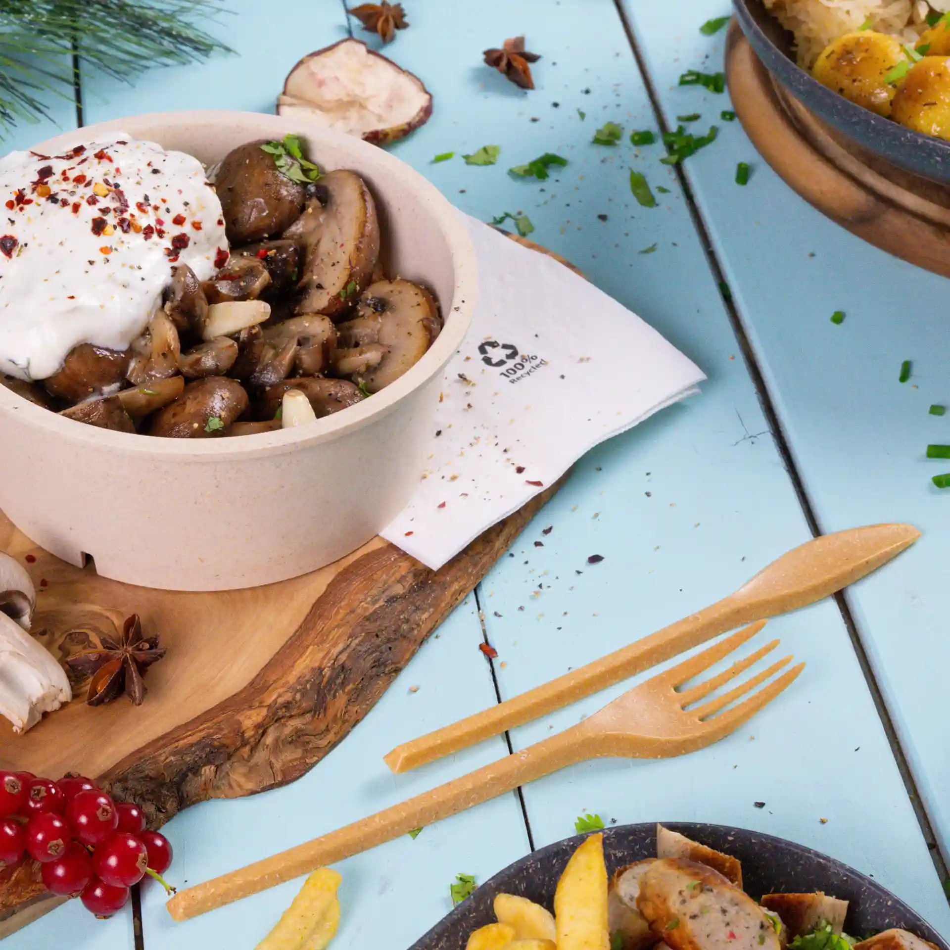 Bol de champignons sautés surmonté de yaourt et d'épices, accompagné d'une fourchette et d'un couteau en bois sur une table bleue.
