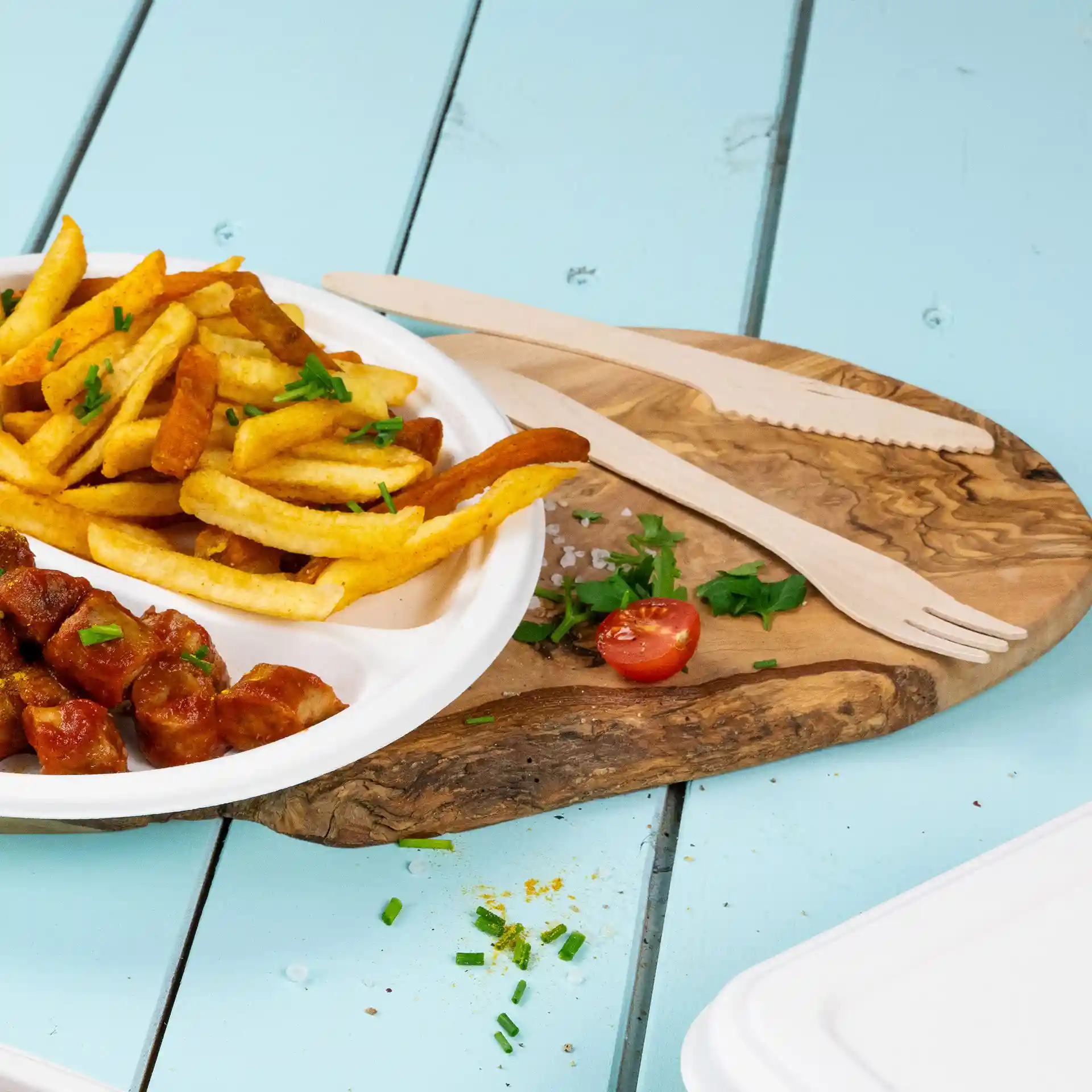 Image d'une assiette de frites et de saucisse, accompagnée d'un couteau et d'une fourchette en bois sur une planche en bois.
