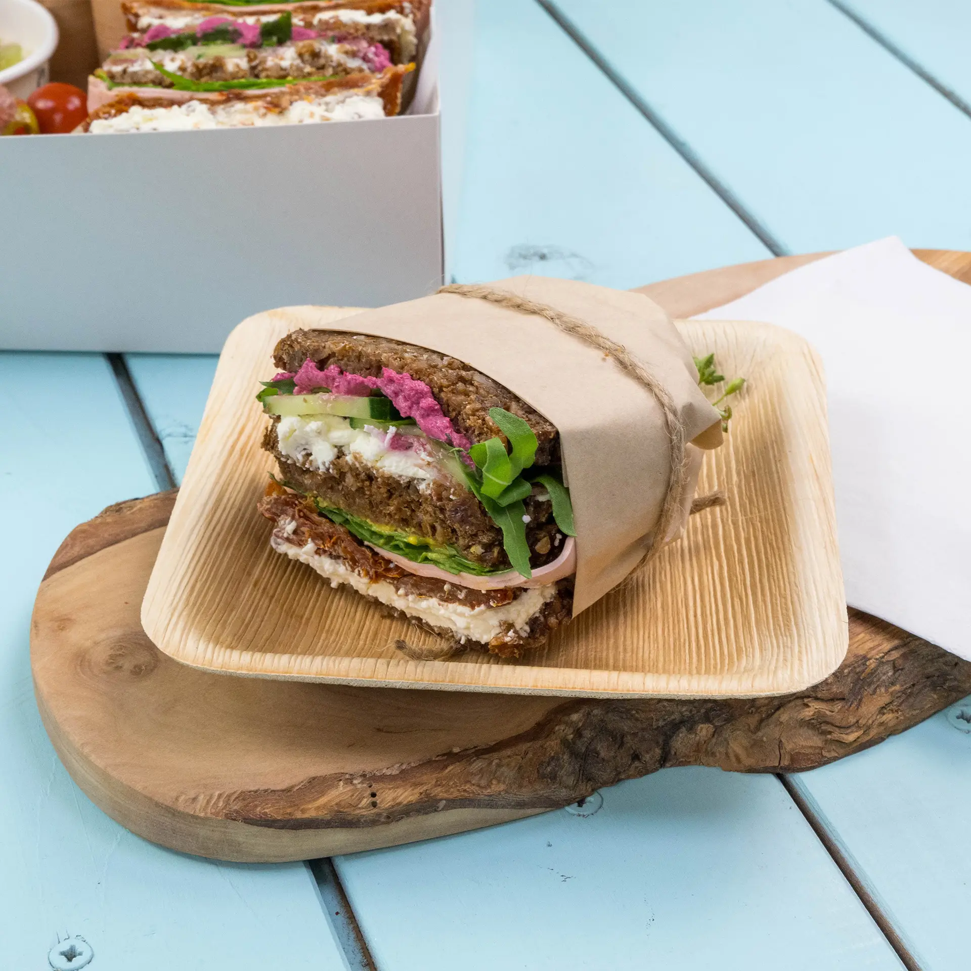 Un sandwich enroulé avec de la roquette verte, une tartinade rose et des couches de légumes, présenté sur une assiette en bois.