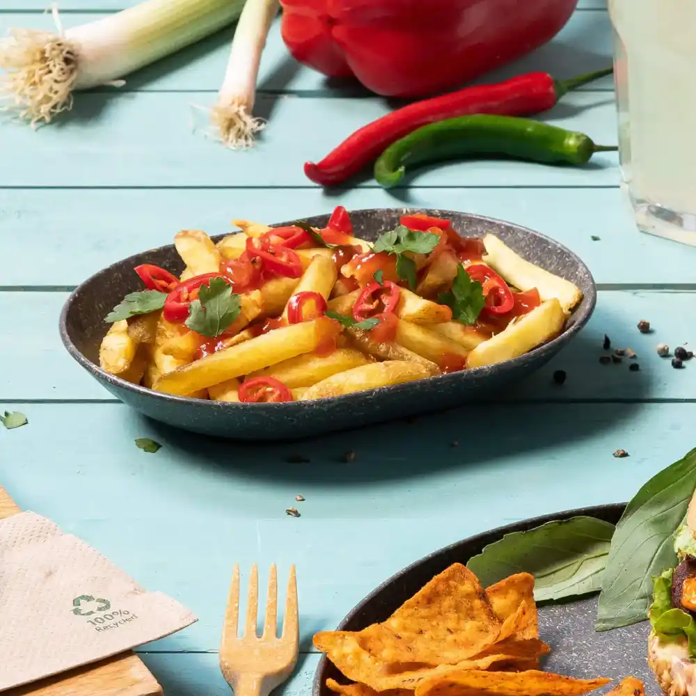 Bol de frites françaises surmonté de piments tranchés et de coriandre sur une table en bois bleu.