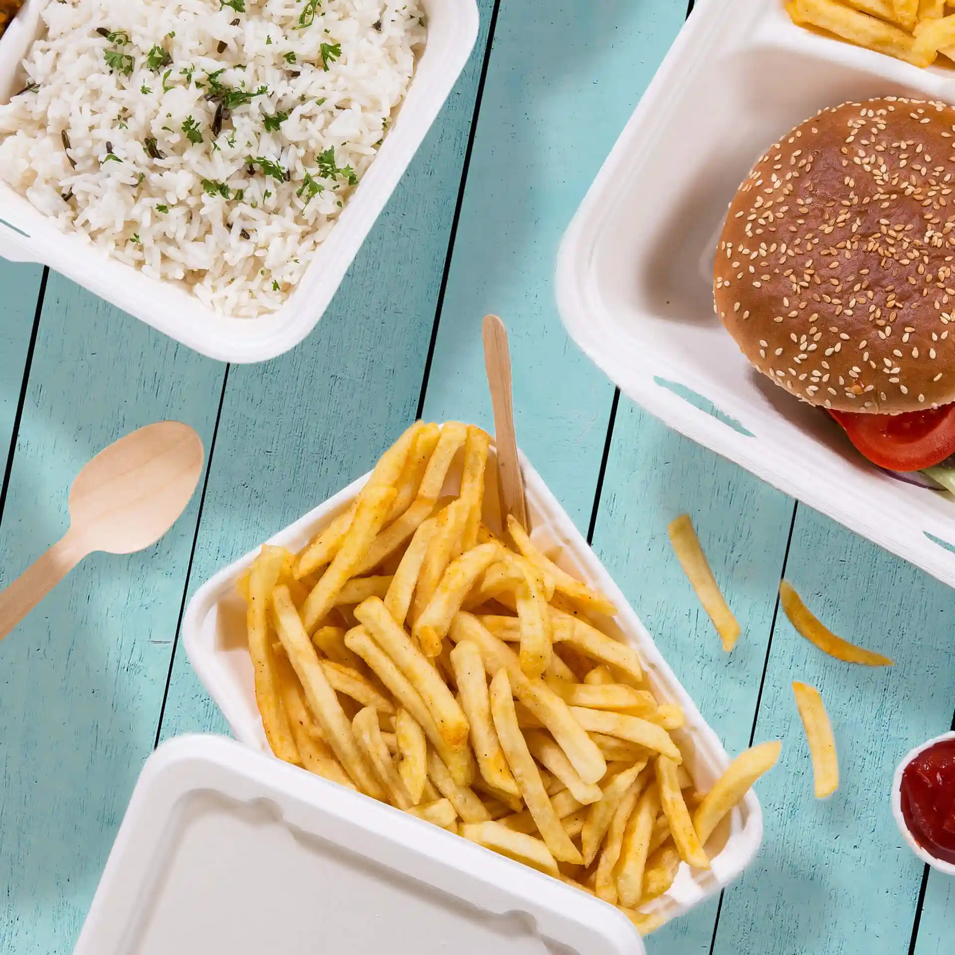 Image d'un bol rectangulaire blanc contenant des frites, avec une cuillère en bois à côté sur une surface en bois bleu.
