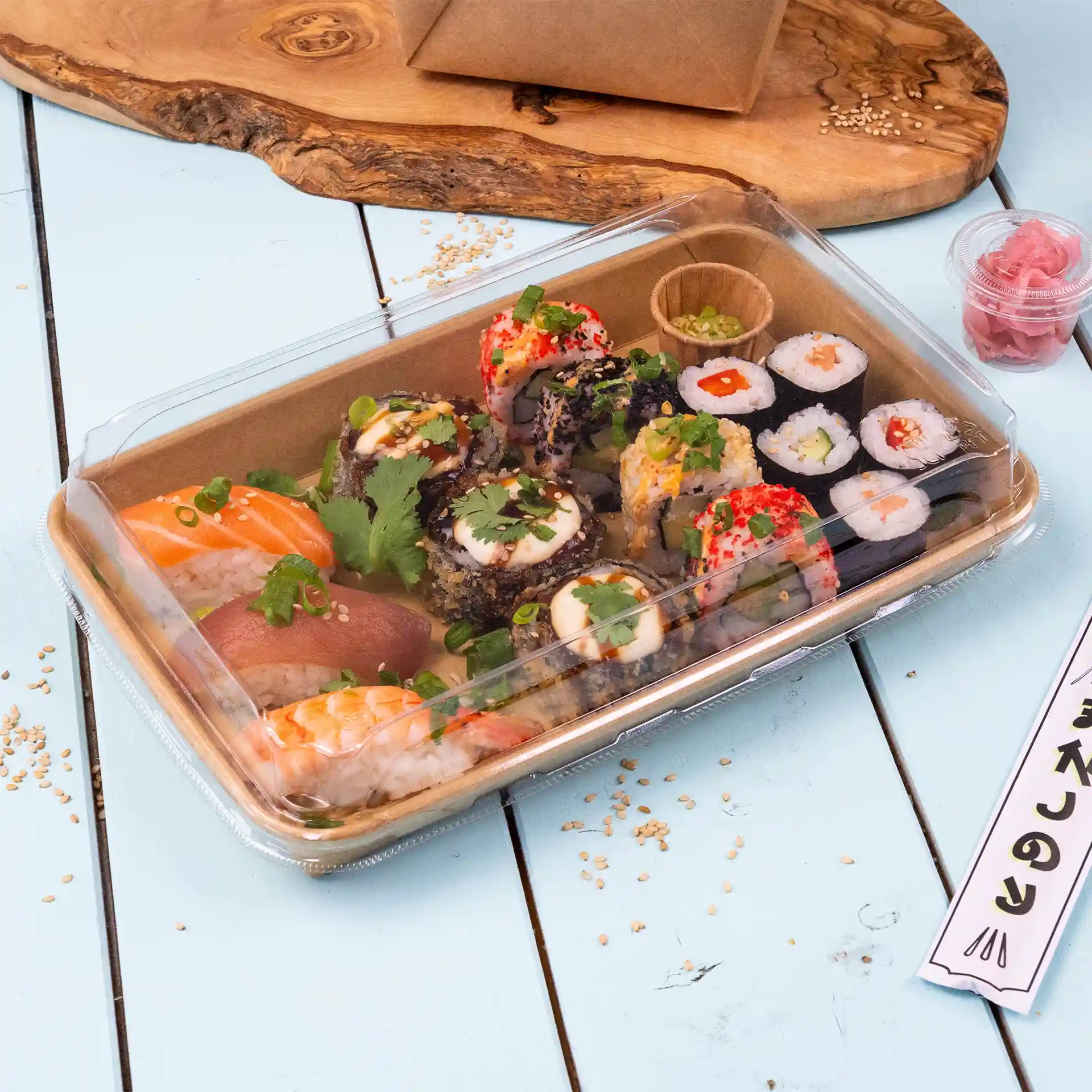 Couvercle transparent de boîte à sushi avec des rouleaux de sushi variés, y compris du saumon et du thon, garni d'herbes et servi avec du gingembre mariné.