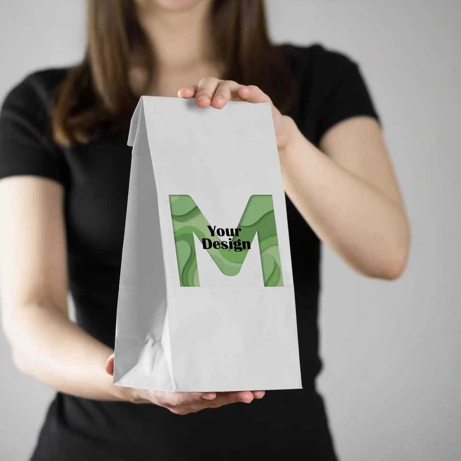 Sac en papier blanc tenu par une personne, avec un design vert portant la lettre 'M' et le texte 'Votre Design'.