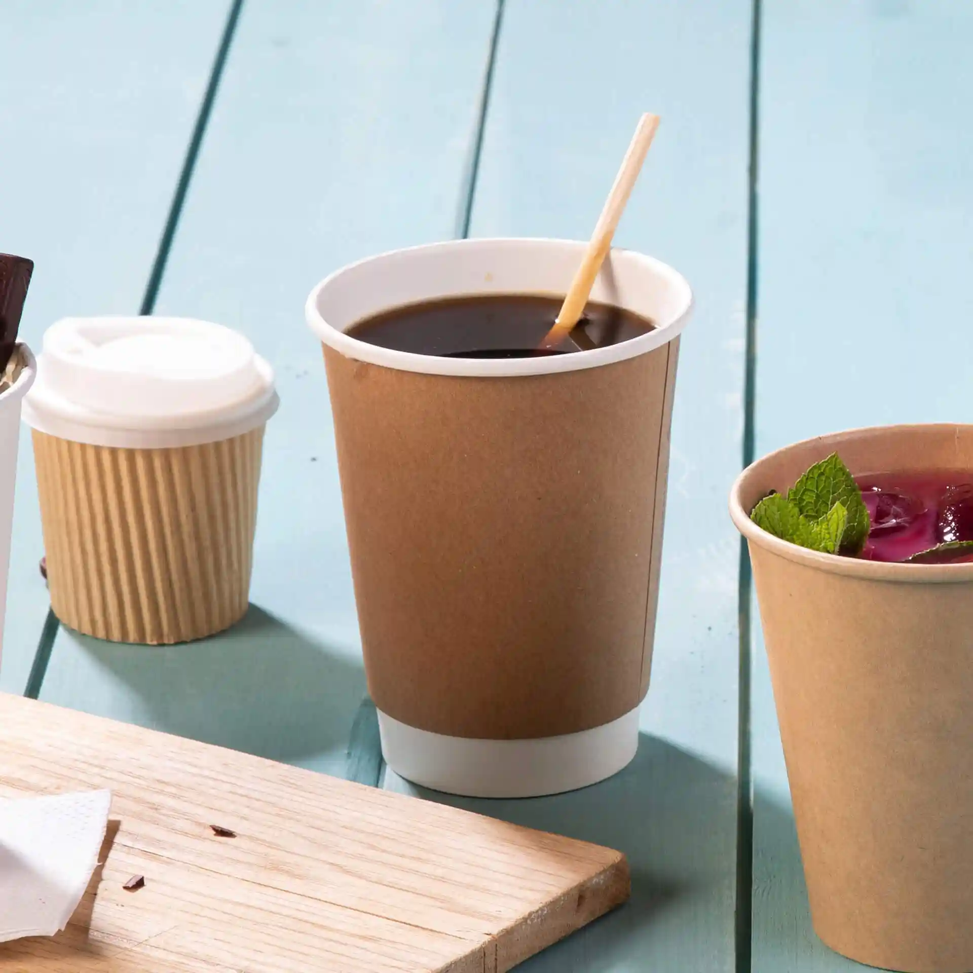 Gobelet en carton double paroi marron avec un intérieur blanc, rempli de café noir et une cuillère en bois.
