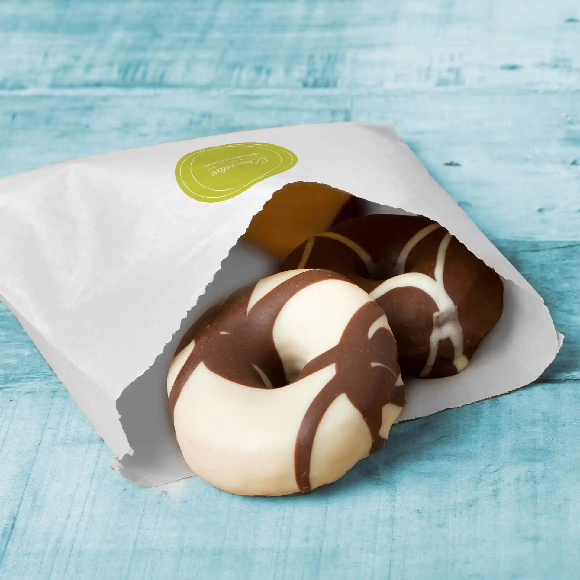 Sac plat blanc partiellement ouvert, révélant deux biscuits ronds avec des designs en chocolat et en glaçage blanc.