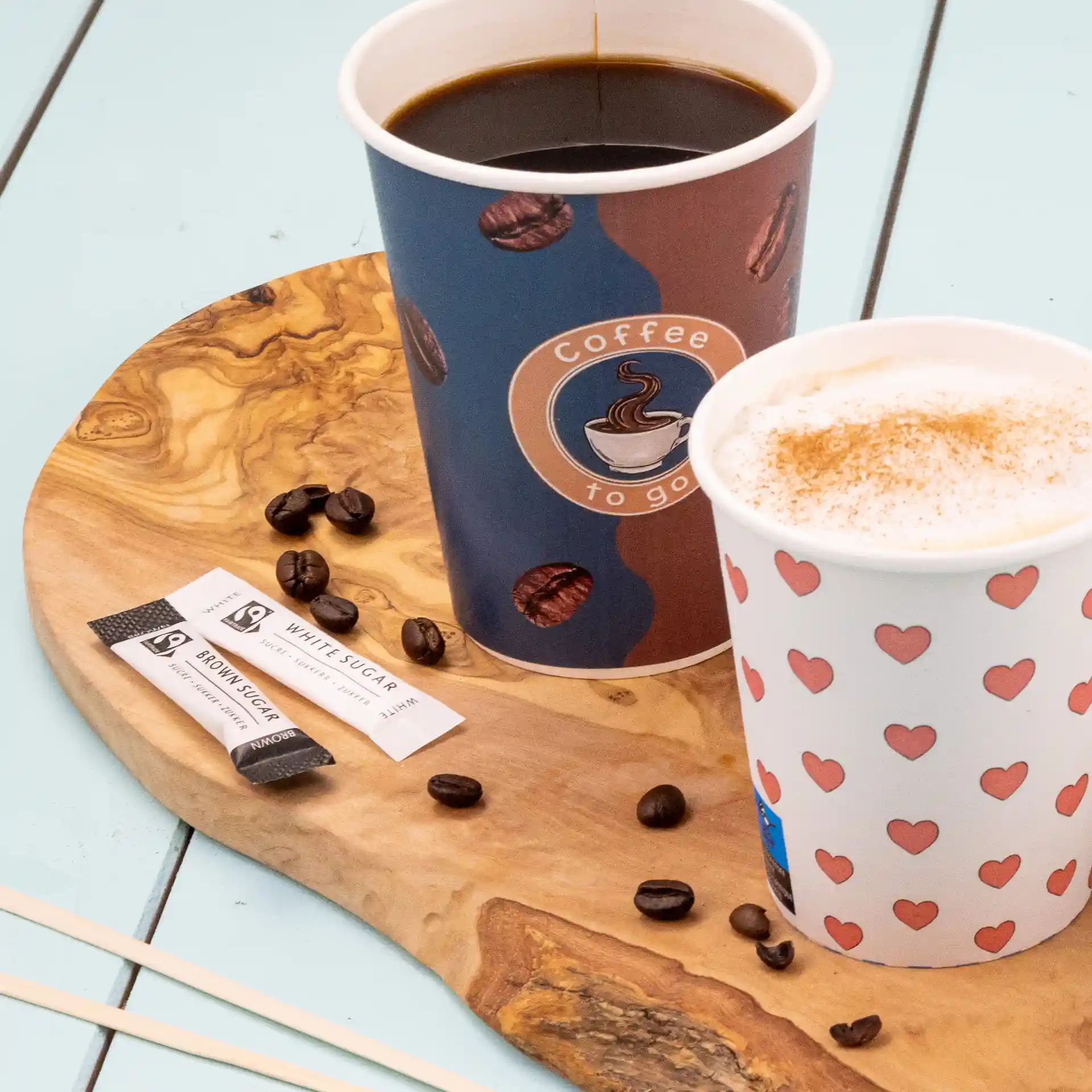 Deux tasses sur une planche en bois avec des bâtonnets de sucre et des grains de café éparpillés.