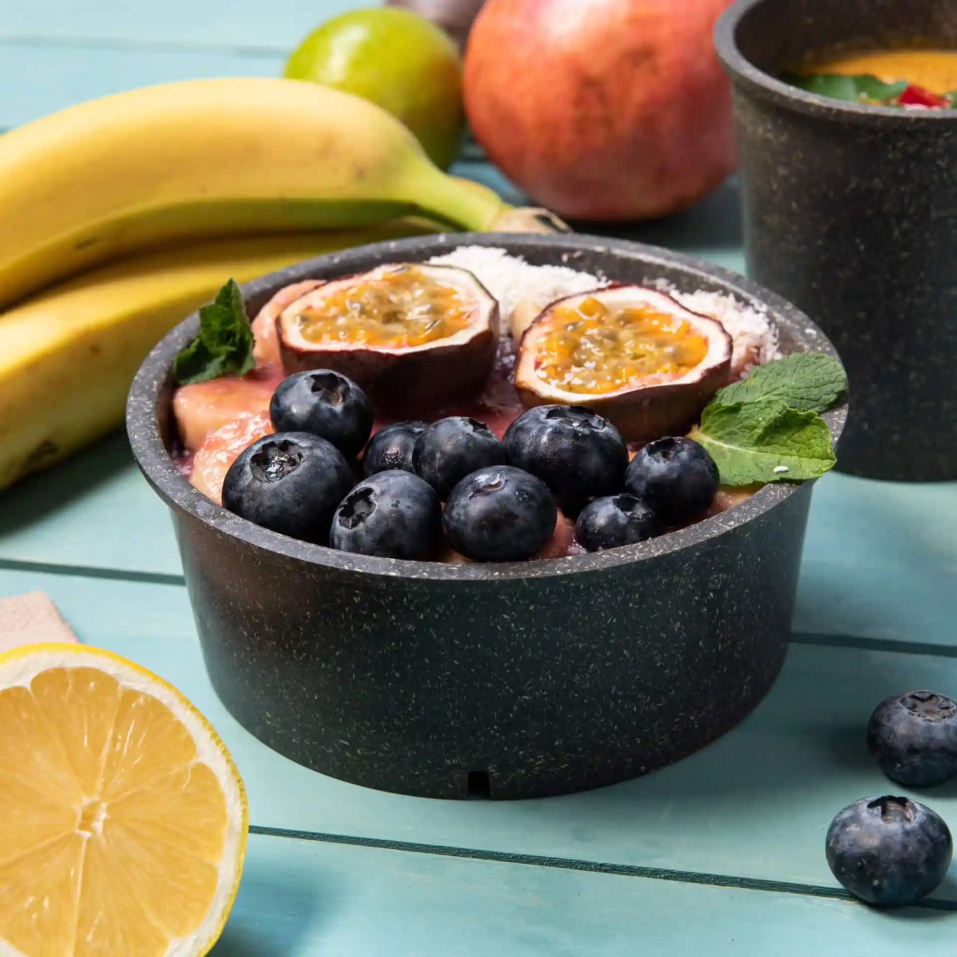 Bol rond gris réutilisable rempli de fruits, y compris des myrtilles et des fruits de la passion, sur une surface en bois.