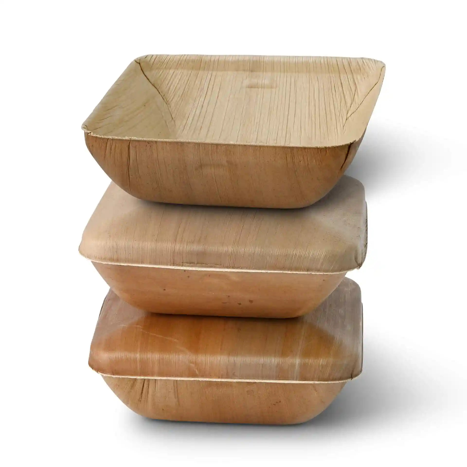 Empilement de trois bols carrés en feuilles de palmier, montrant la texture du grain naturel, avec le bol du dessus légèrement incliné.