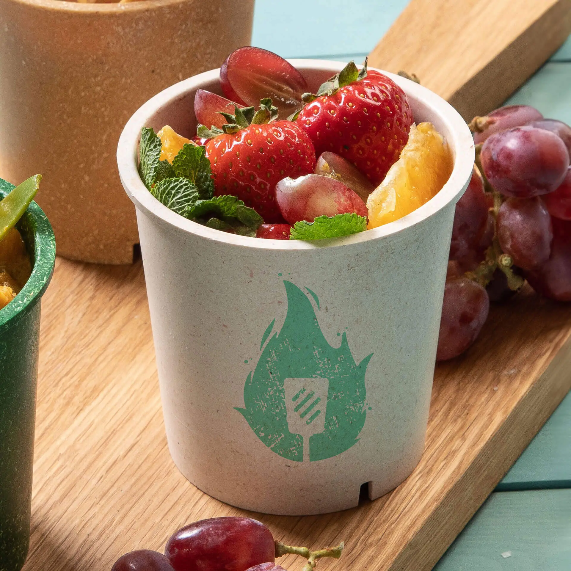 Une tasse à soupe réutilisable blanc crème remplie de soupe jaune, garnie de ciboulette hachée ; une cuillère à côté.