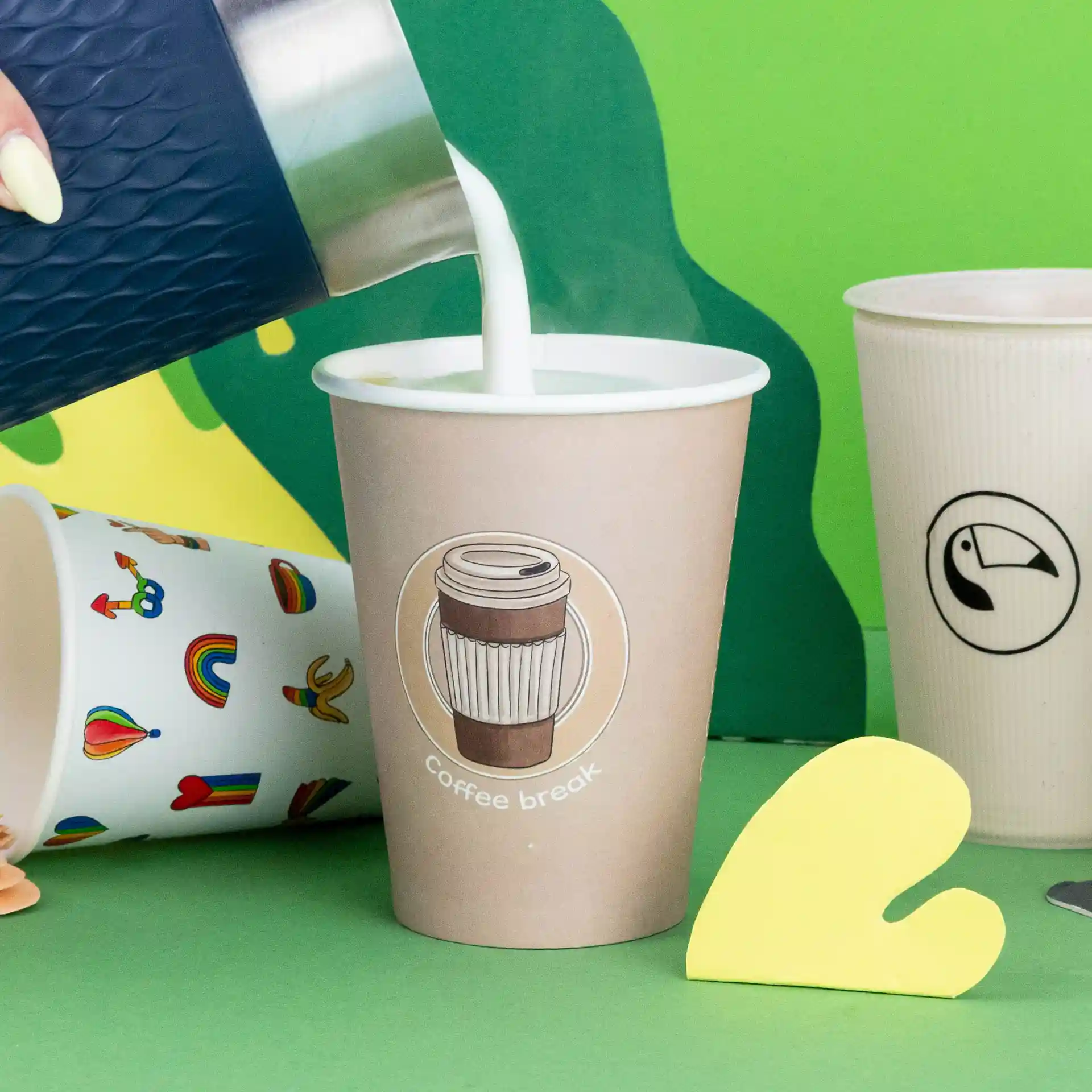 Image d'un gobelet avec un logo "pause café", rempli de lait, entouré d'autres gobelets sur un fond coloré.