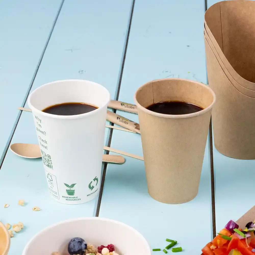 Deux tasses avec du café, l'une blanche et l'autre brune, à côté de bâtonnets en bois sur une surface bleue.