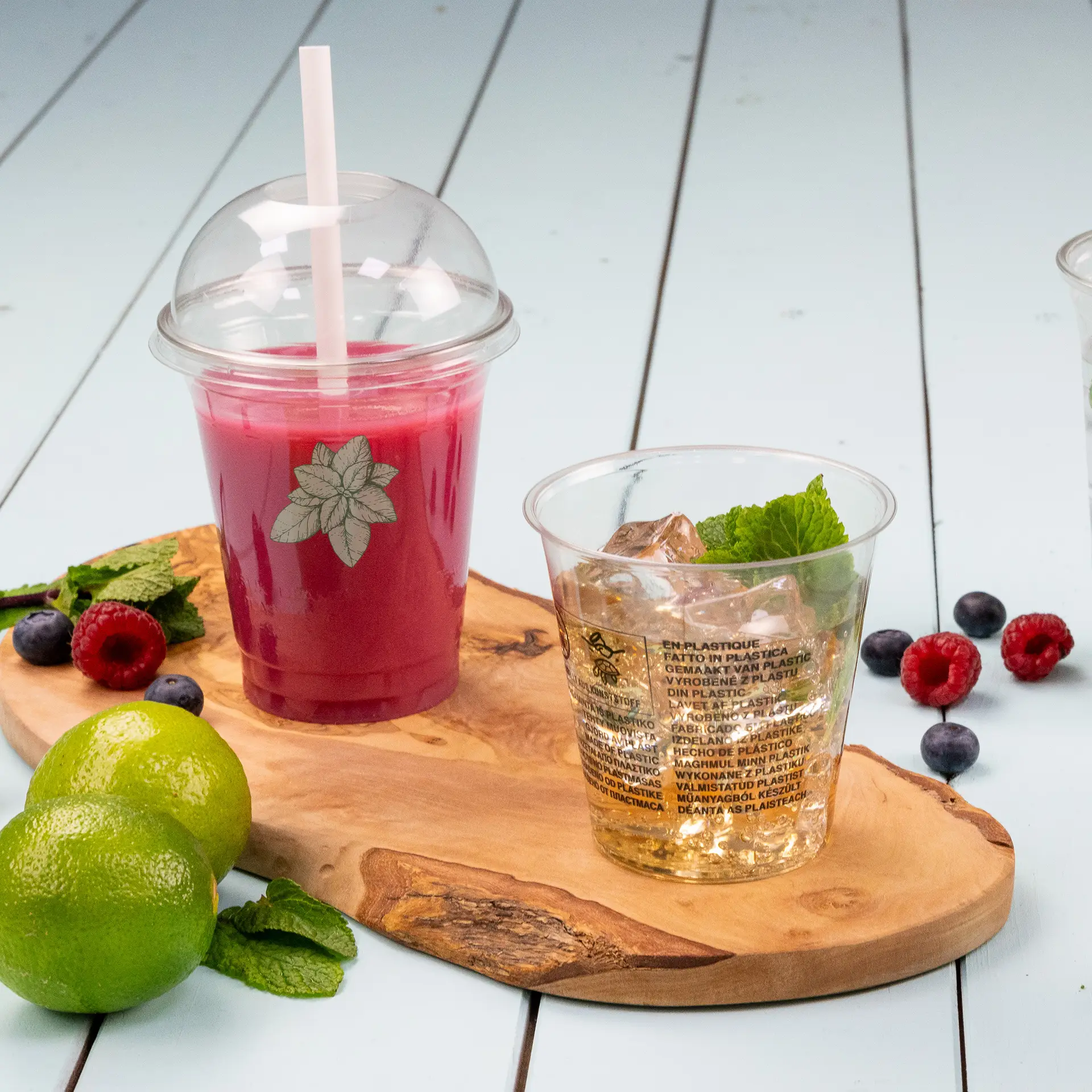 Gobelet rPET transparent pour boissons froides, avec un motif feuillu, à côté d'un deuxième gobelet sur une planche en bois ; garni de menthe et de citron vert.