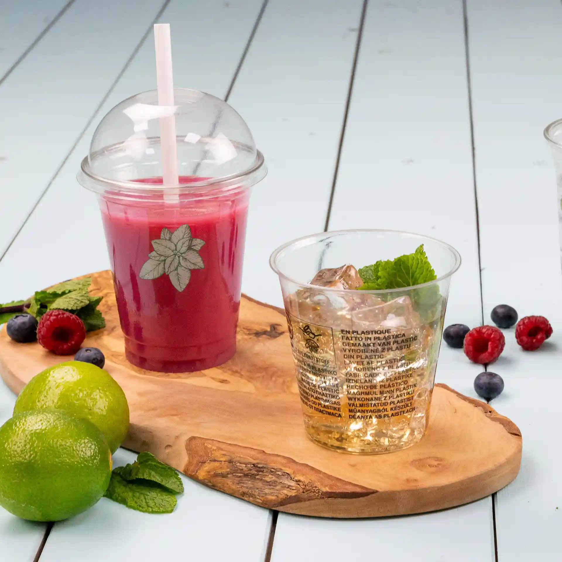 Gobelet rPET transparent de 12 oz avec couvercle en dôme et paille, rempli d'une boisson rouge, à côté d'un gobelet de glace et de menthe.