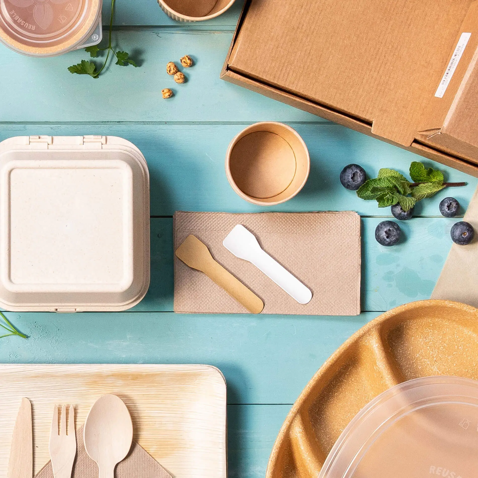 Image de divers contenants alimentaires jetables, ustensiles et une boîte en carton sur une surface bleue.