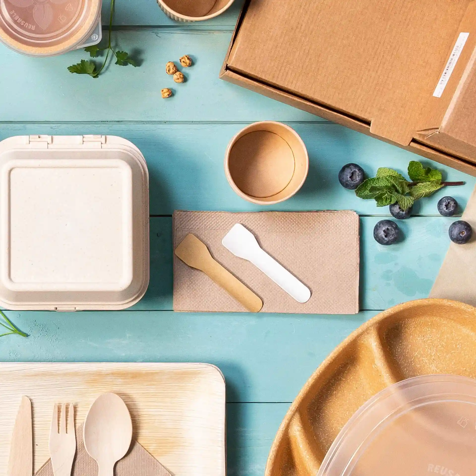 Image de divers contenants alimentaires jetables, ustensiles et une boîte en carton sur une surface bleue.