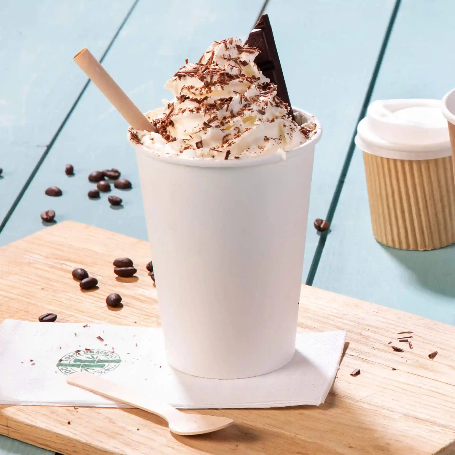 Gobelet blanc rempli de crème fouettée et de copeaux de chocolat, avec une cuillère en bois à côté sur une surface en bois.