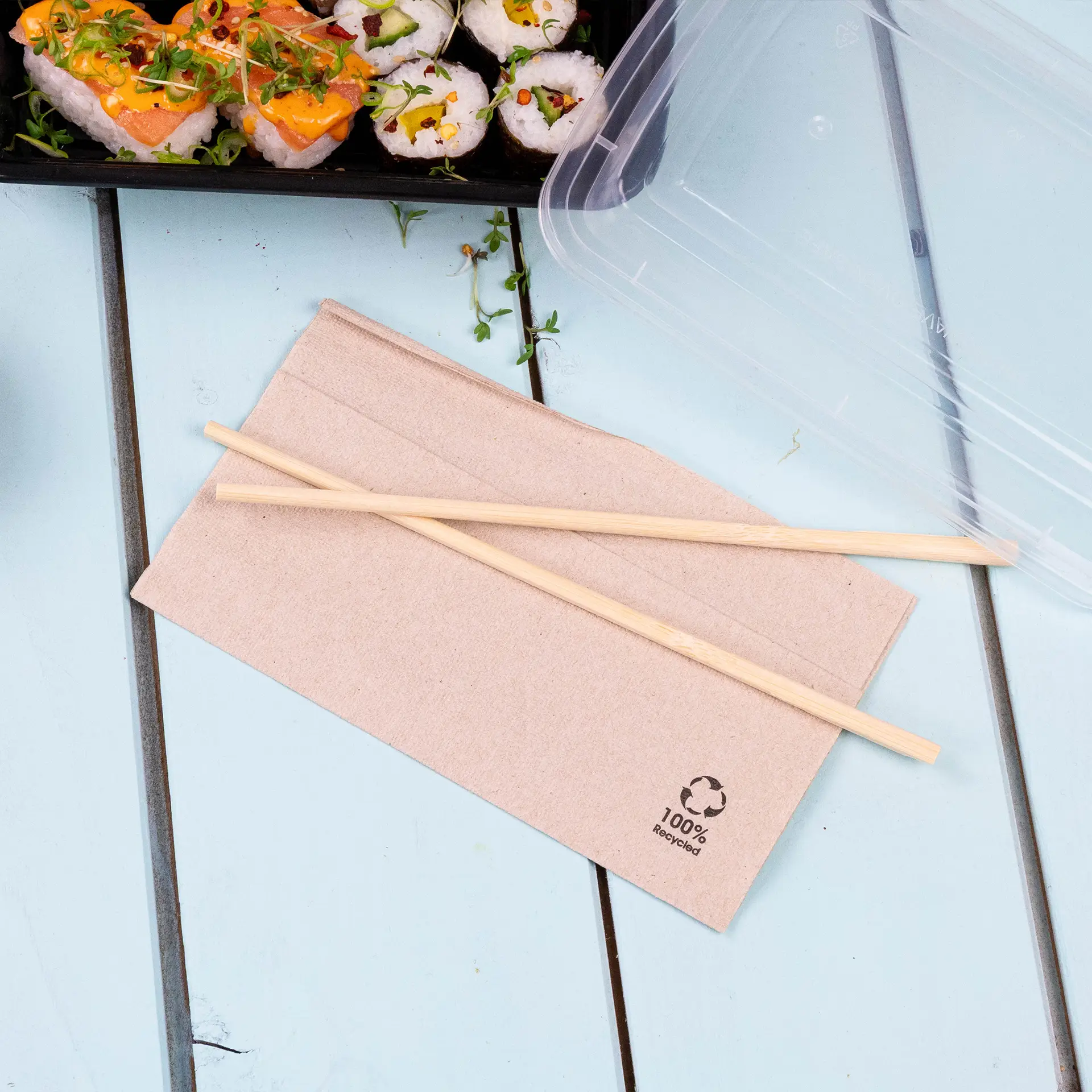 Serviette en papier recyclé avec logo de recyclage subtil et baguettes en bois sur une table bleue, à côté de sushis dans un contenant en plastique.