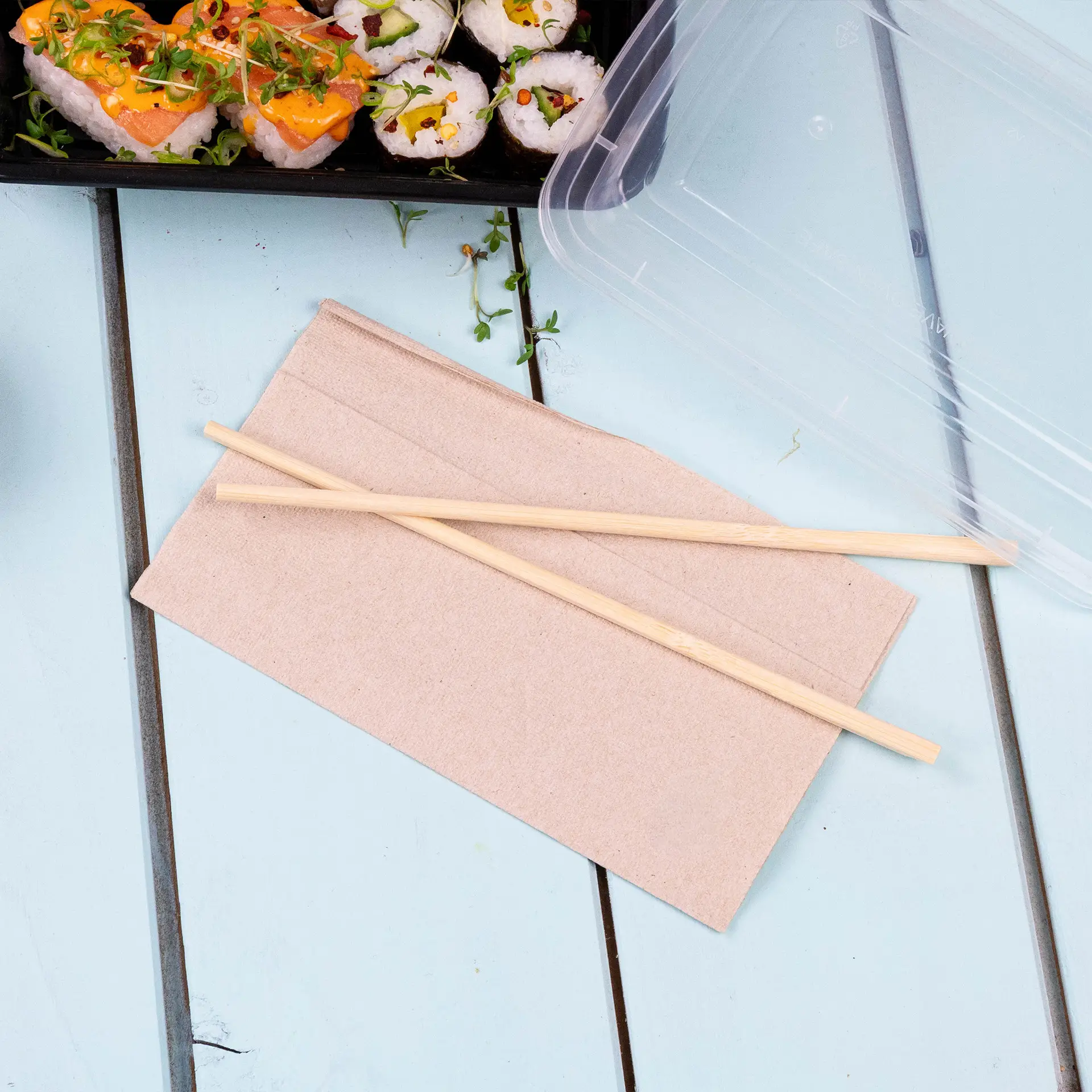 Serviette en papier de couleur non blanchie avec deux baguettes en bois posées dessus, sur une surface bleu clair.