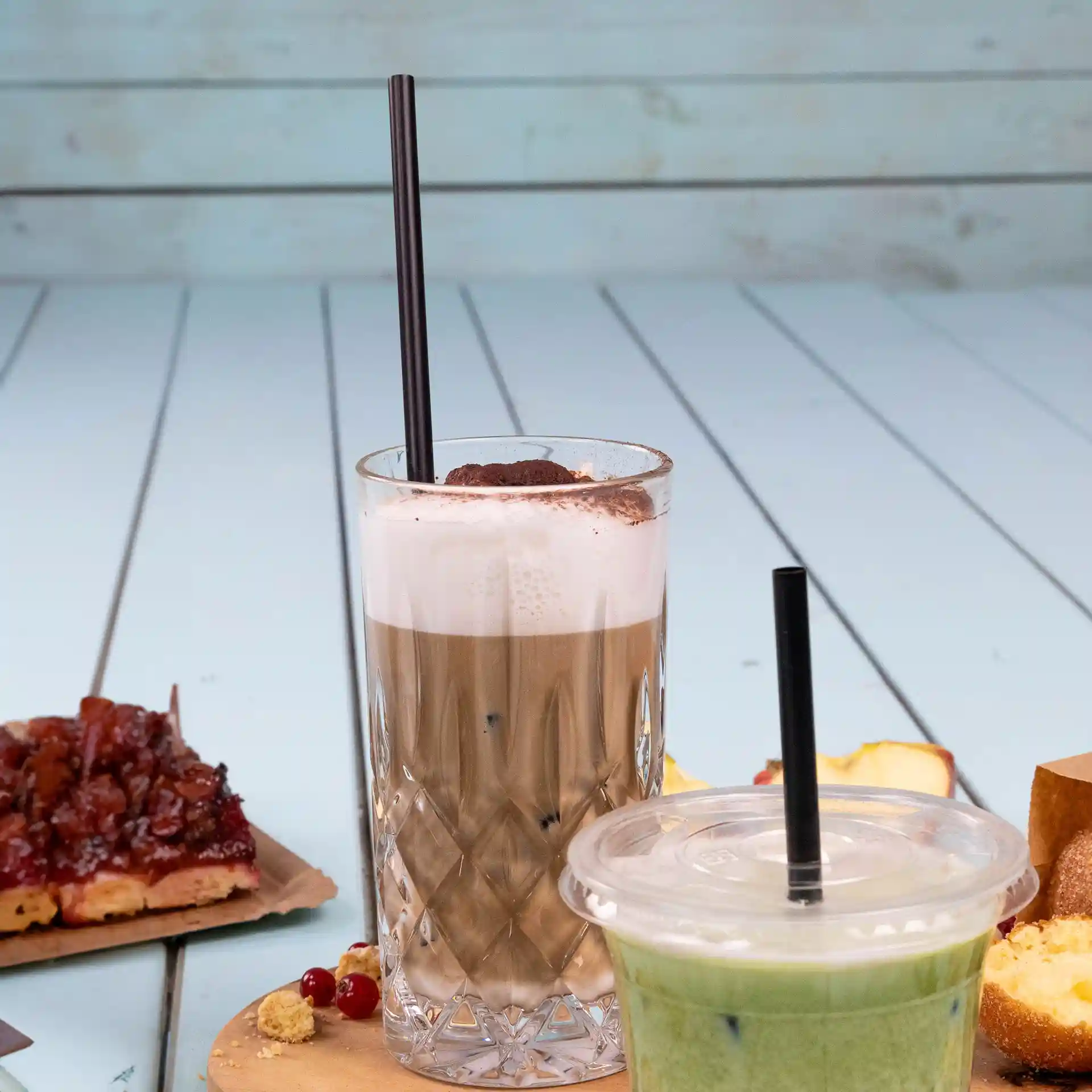 Image de deux boissons avec des pailles réutilisables noires, l'une dans un verre transparent et l'autre dans un gobelet en plastique, sur une table en bois.
