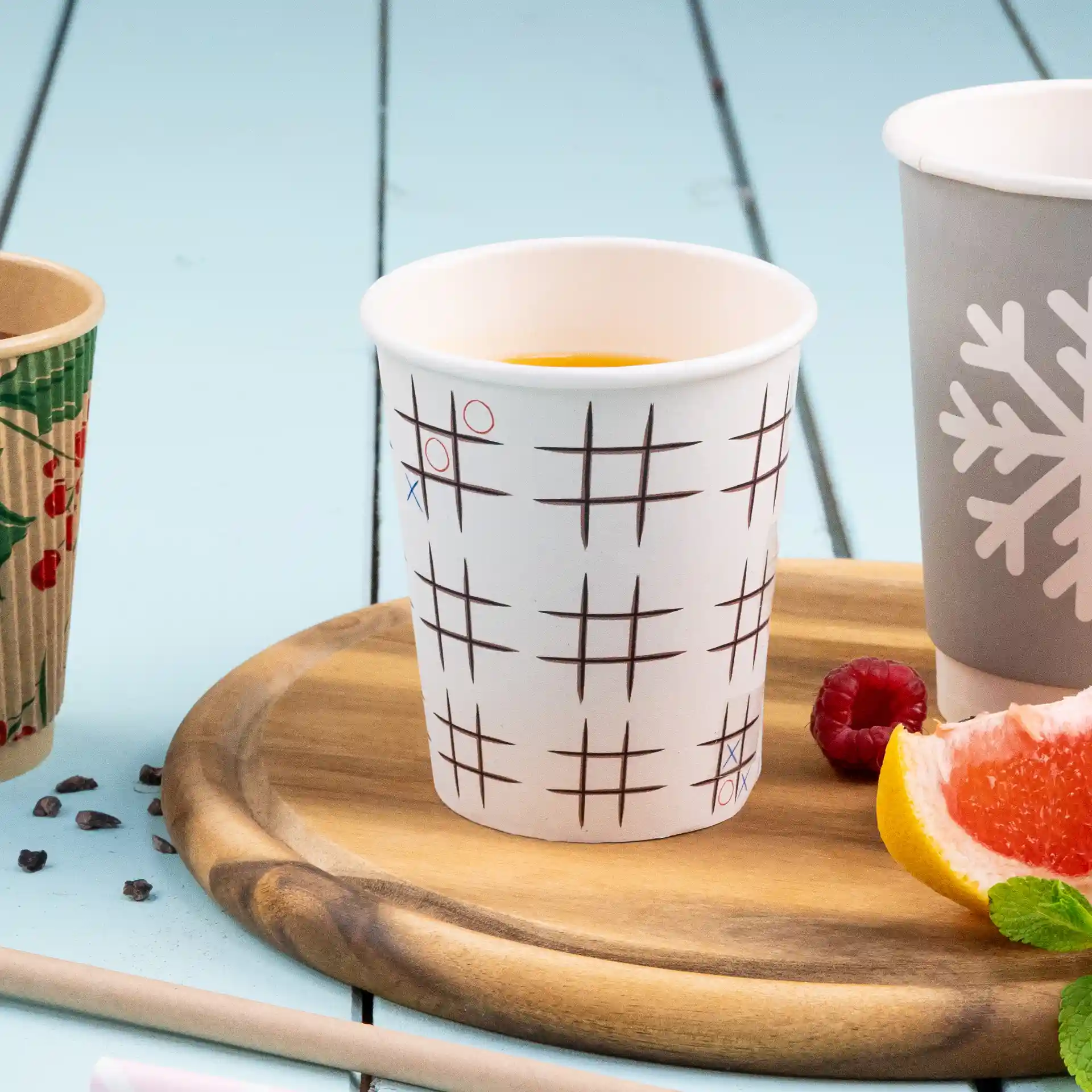 Gobelet blanc avec un motif de morpion, placé sur un plateau en bois avec des fruits et un autre gobelet à proximité.