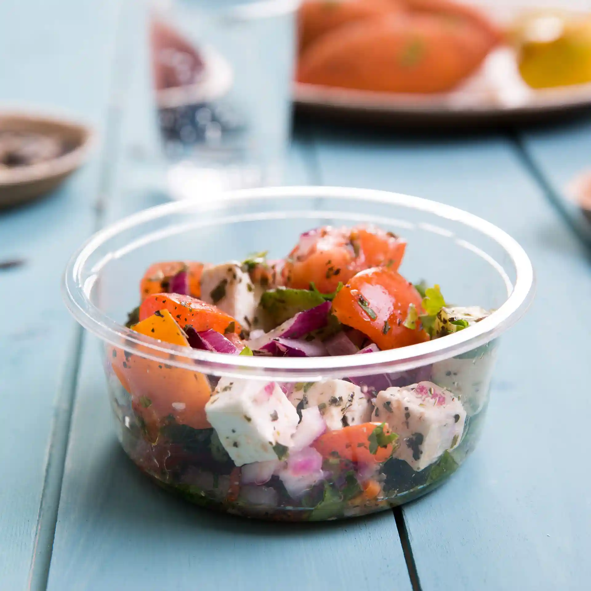 Conteneur rond transparent rempli de salade, avec des tomates, des oignons et des herbes.